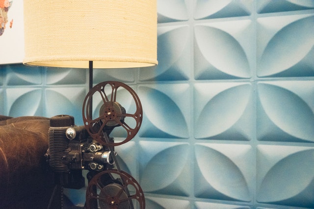 Lampa vyrobená zo starej kamery vedľa koženého gauča a steny s modrým obkladom